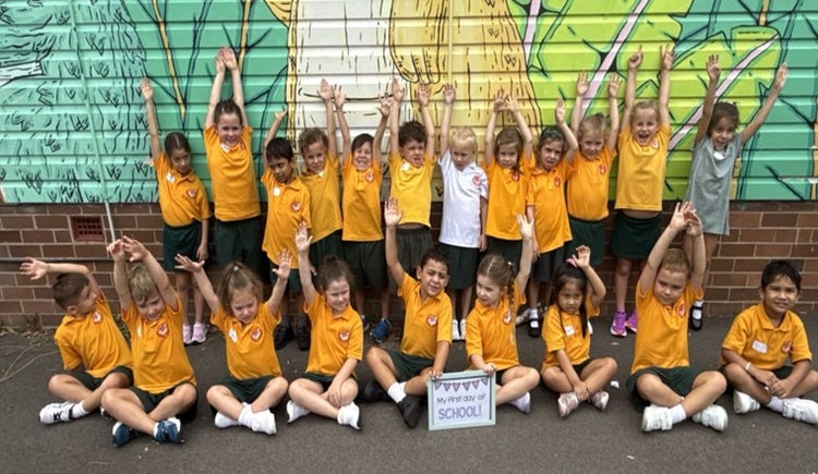 Kindergarten class in front of painted wall with their arms raised on their first day of school