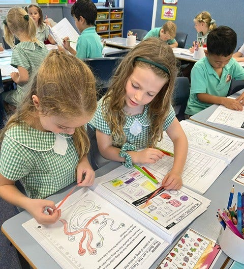 Two students in the classroom working at a desk together in their work books