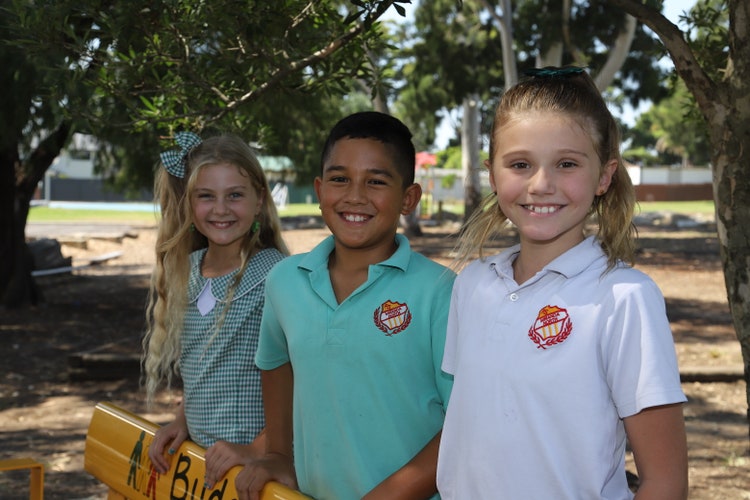 Three students standing at the buddy bench with the back grass area in the background